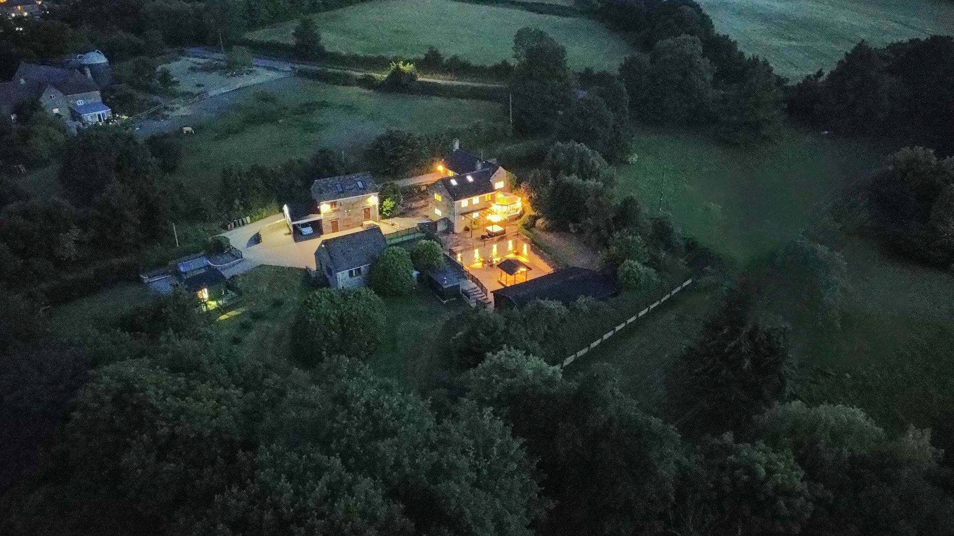 Aerial view of a house illuminated at night, surrounded by dark trees and a grassy field Habberjam farm 
