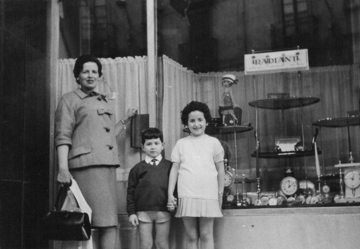 Una fotografía en blanco y negro de una mujer y dos niños de pie frente a la ventana de una tienda.