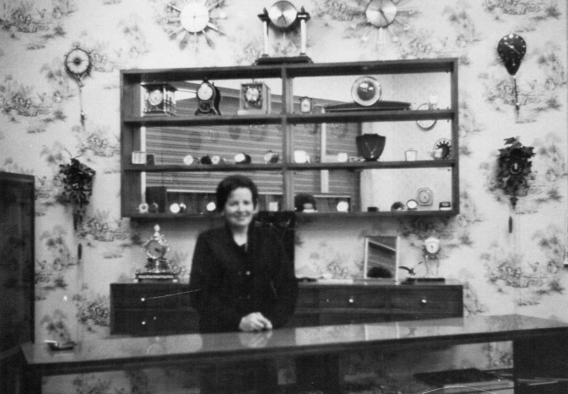 Una fotografía en blanco y negro de una mujer detrás de un mostrador en una tienda.