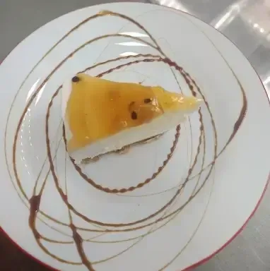 Una porción de tarta de queso con maracuyá en un plato blanco decorado con espirales de sirope de chocolate.