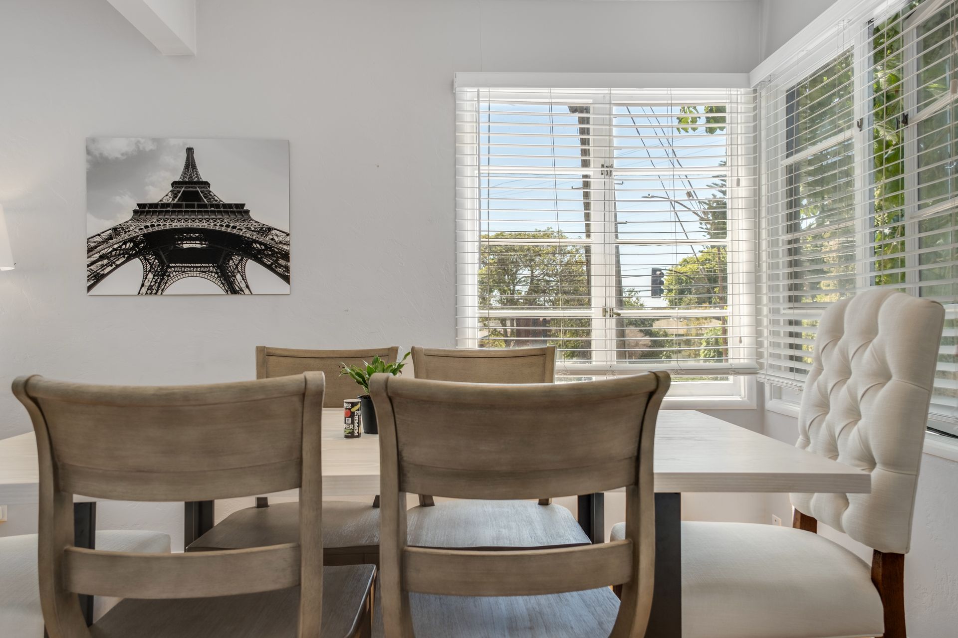 A dining room with a table and chairs and a picture of the eiffel tower on the wall.