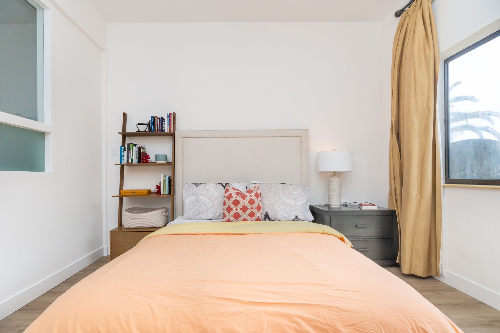 A bedroom with a bed , nightstand , lamp and window.