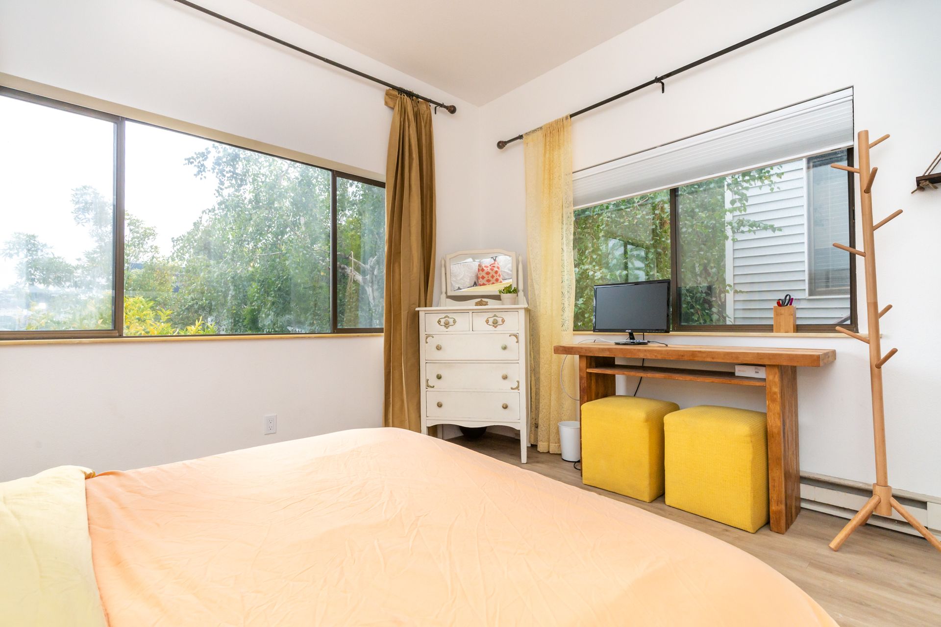 A bedroom with a bed , dresser , desk , and two yellow ottomans.