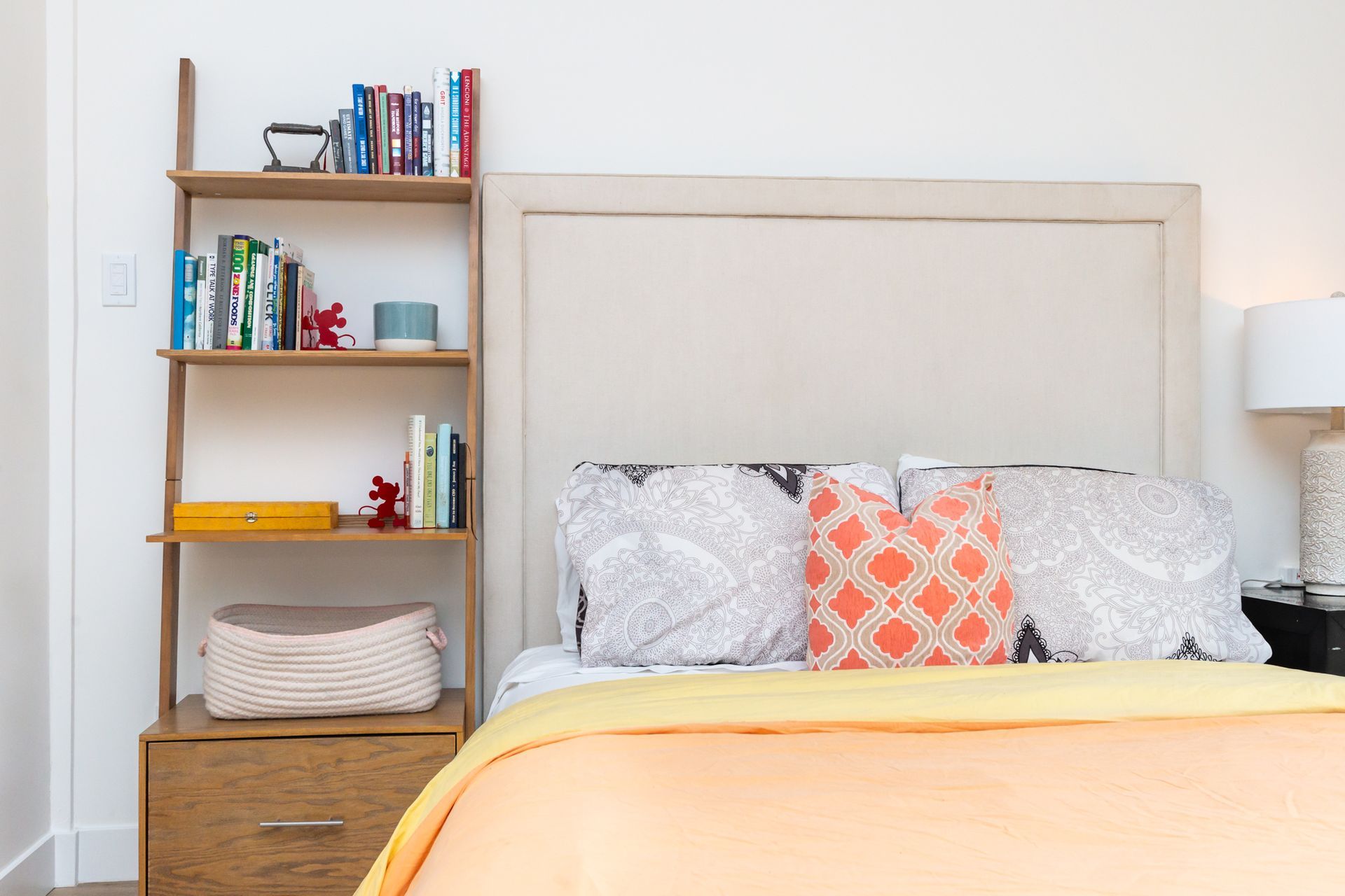 A bedroom with a bed , nightstand , bookshelf and lamp.