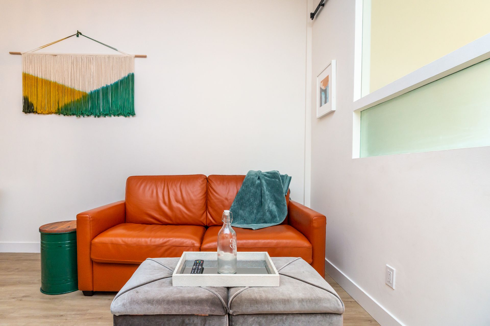 A living room with a couch , ottoman , table and window.