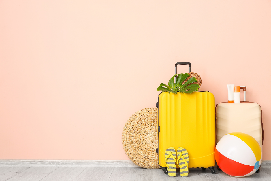 Yellow and tan suitcases packed for travel with beach accessories against a peach wall.