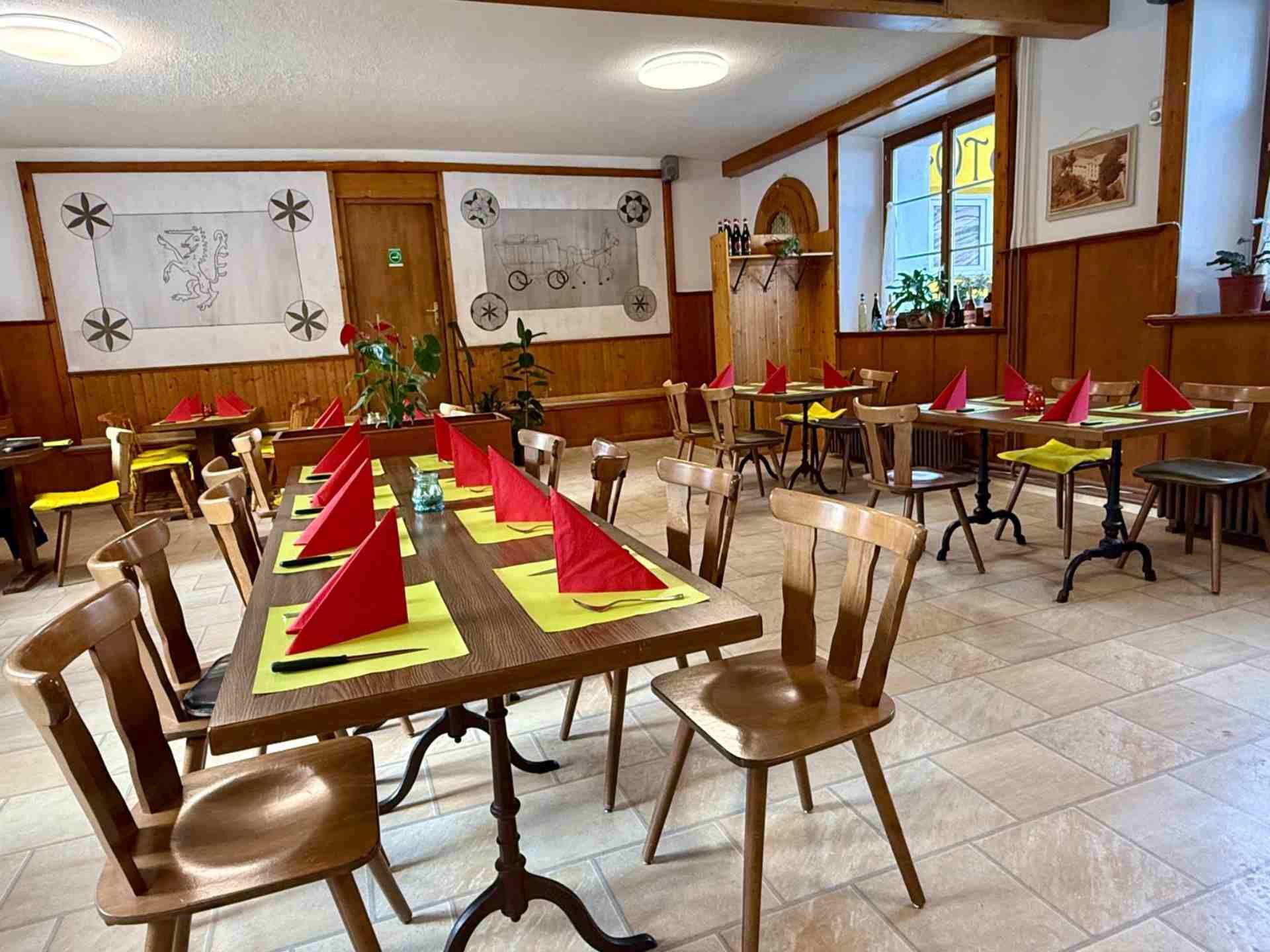 Esszimmer mit Holztischen, Stühlen und roten Servietten. Helle Wände, Kunstwerke und Fenster.