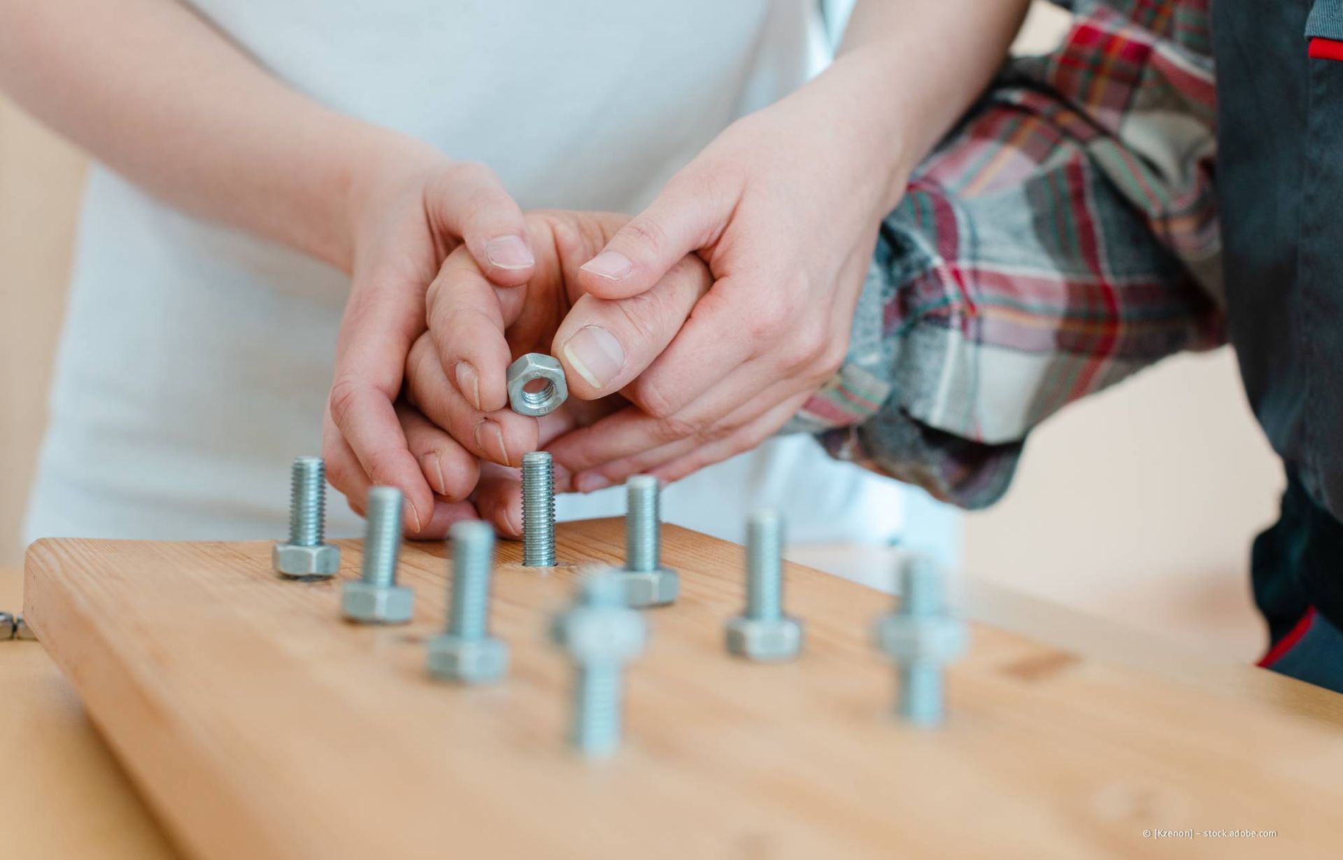 Hände halten eine Mutter und setzen sie auf einen Bolzen auf einem Holzbrett.