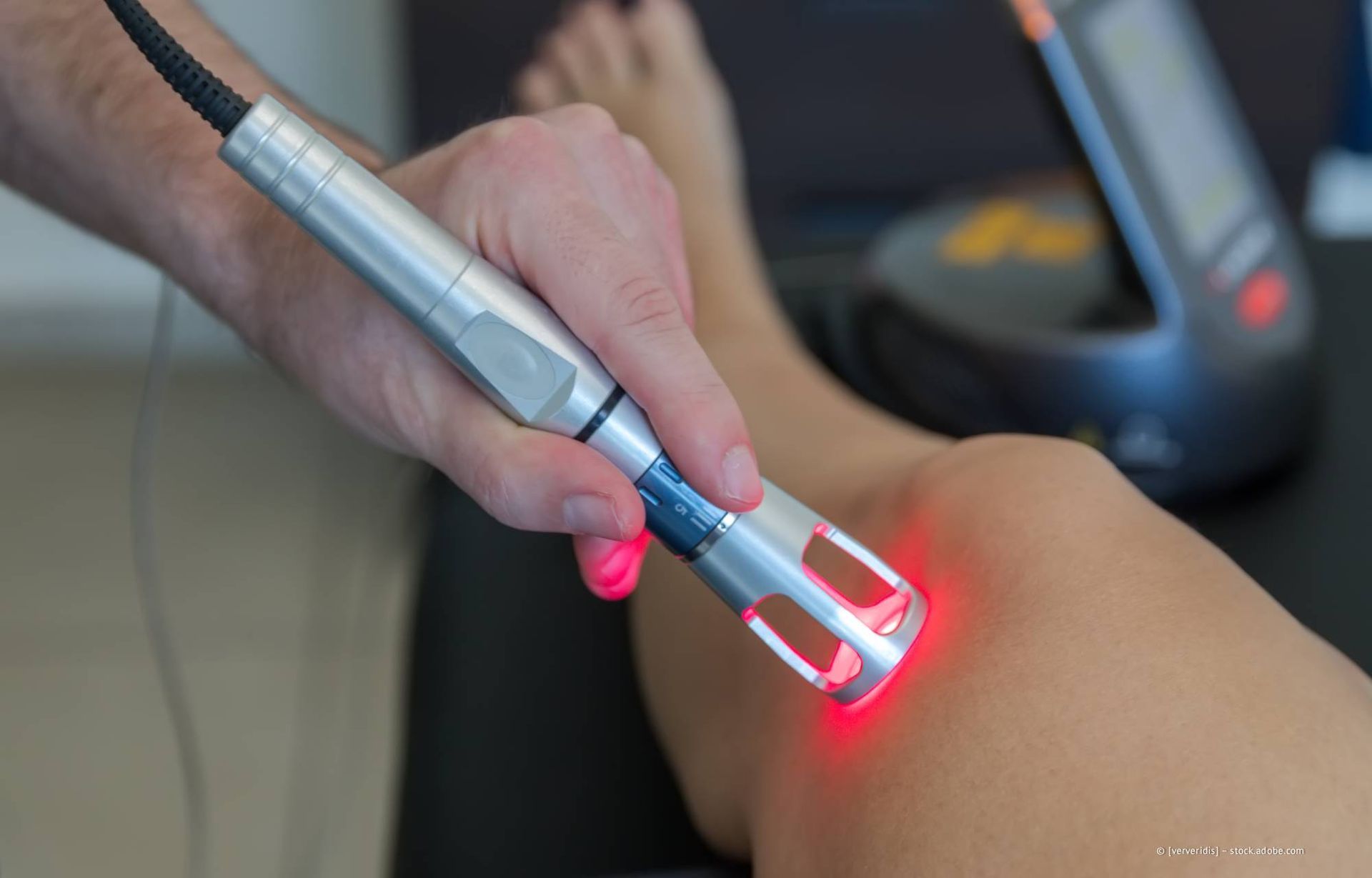 Eine Lasertherapie wird am Knie angewendet. Das Gerät strahlt rotes Licht aus.