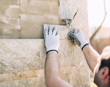 Un hombre que lleva guantes está colocando azulejos en una pared.