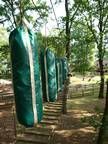 Eine Reihe grüner Boxsäcke hängt an Bäumen in einem Park.