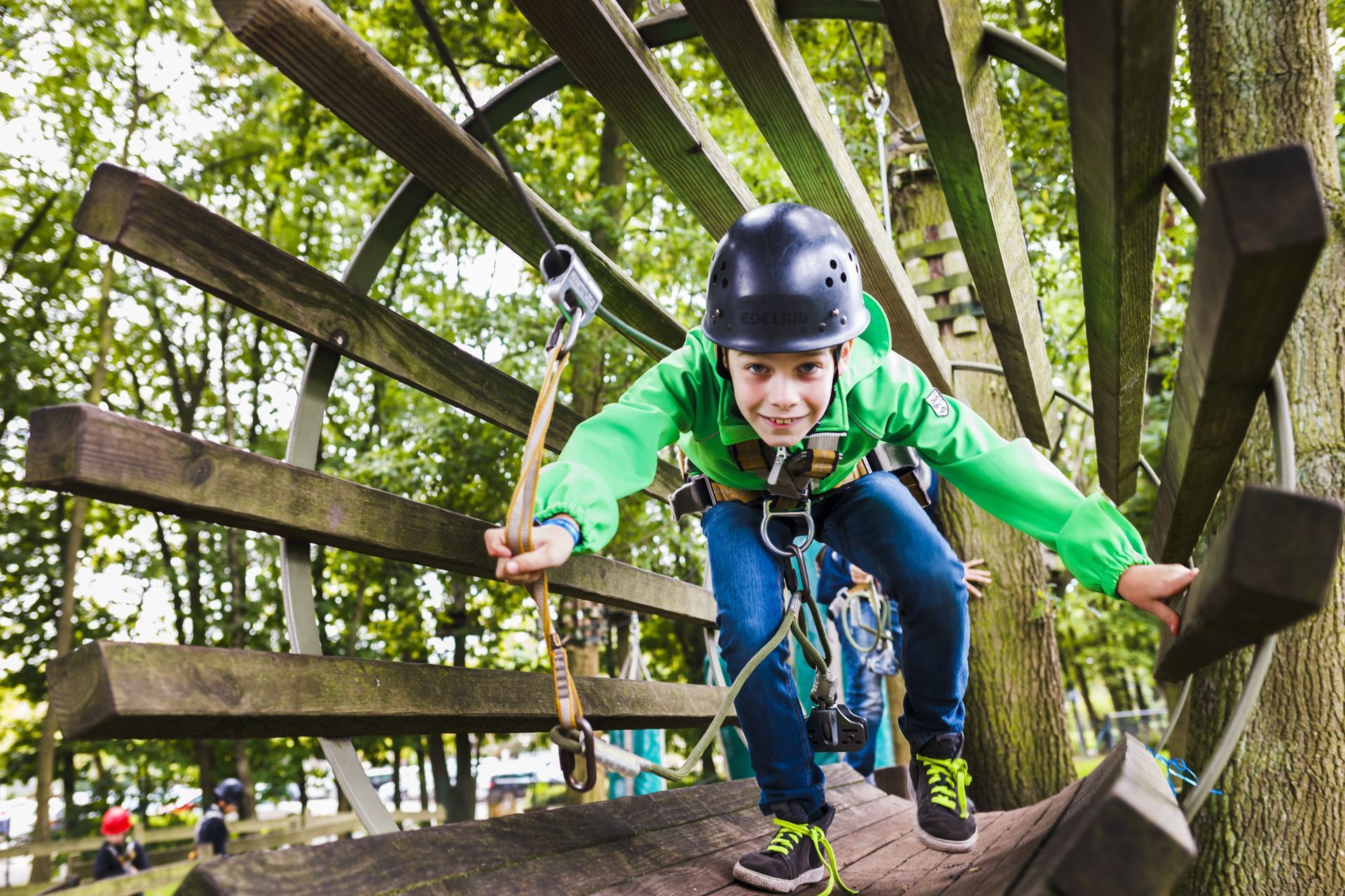 Ein kleiner Junge mit Helm klettert auf eine Holzkonstruktion.
