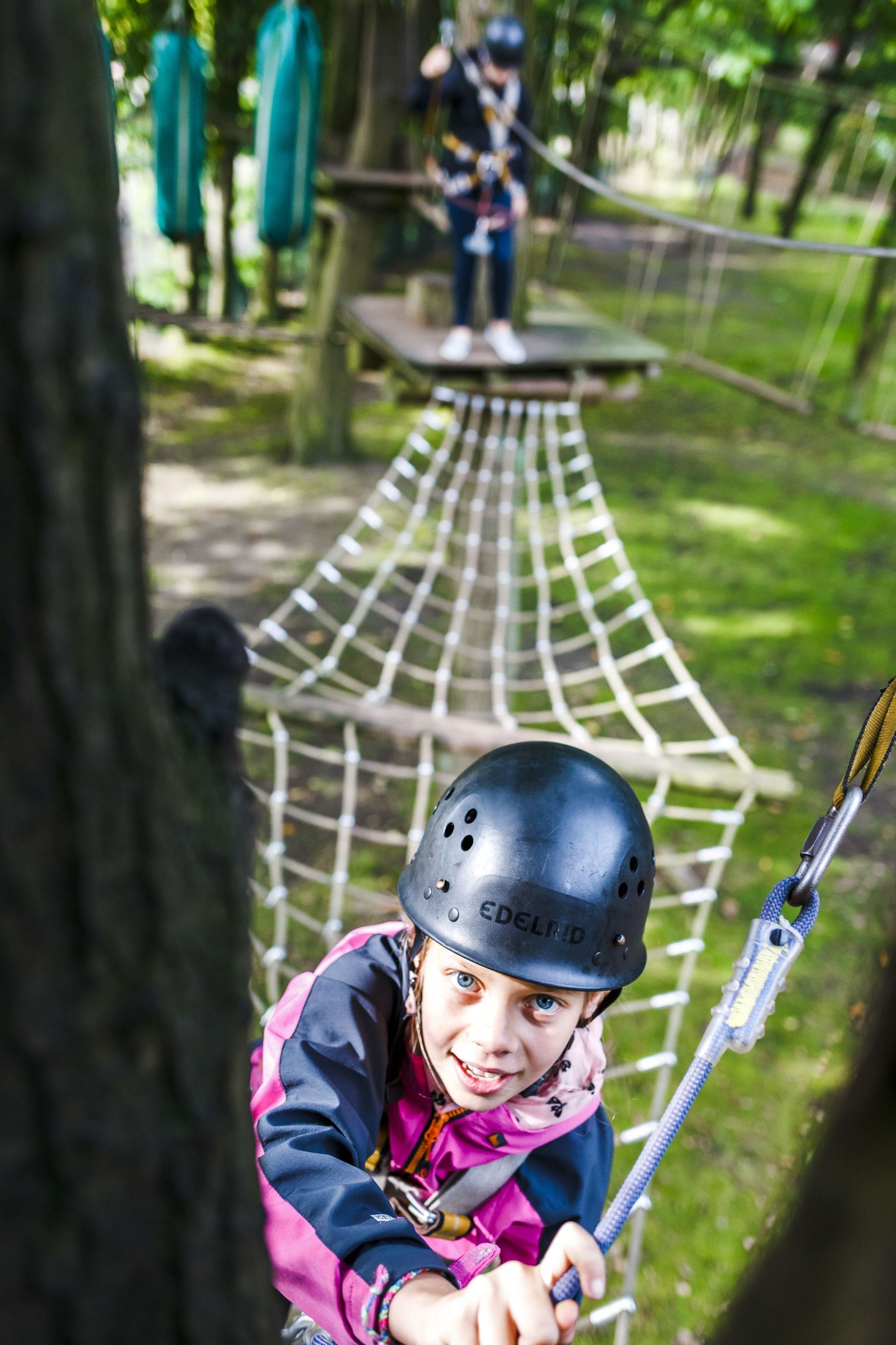 Ein kleines Mädchen klettert in einem Park auf einem Hochseilgarten.