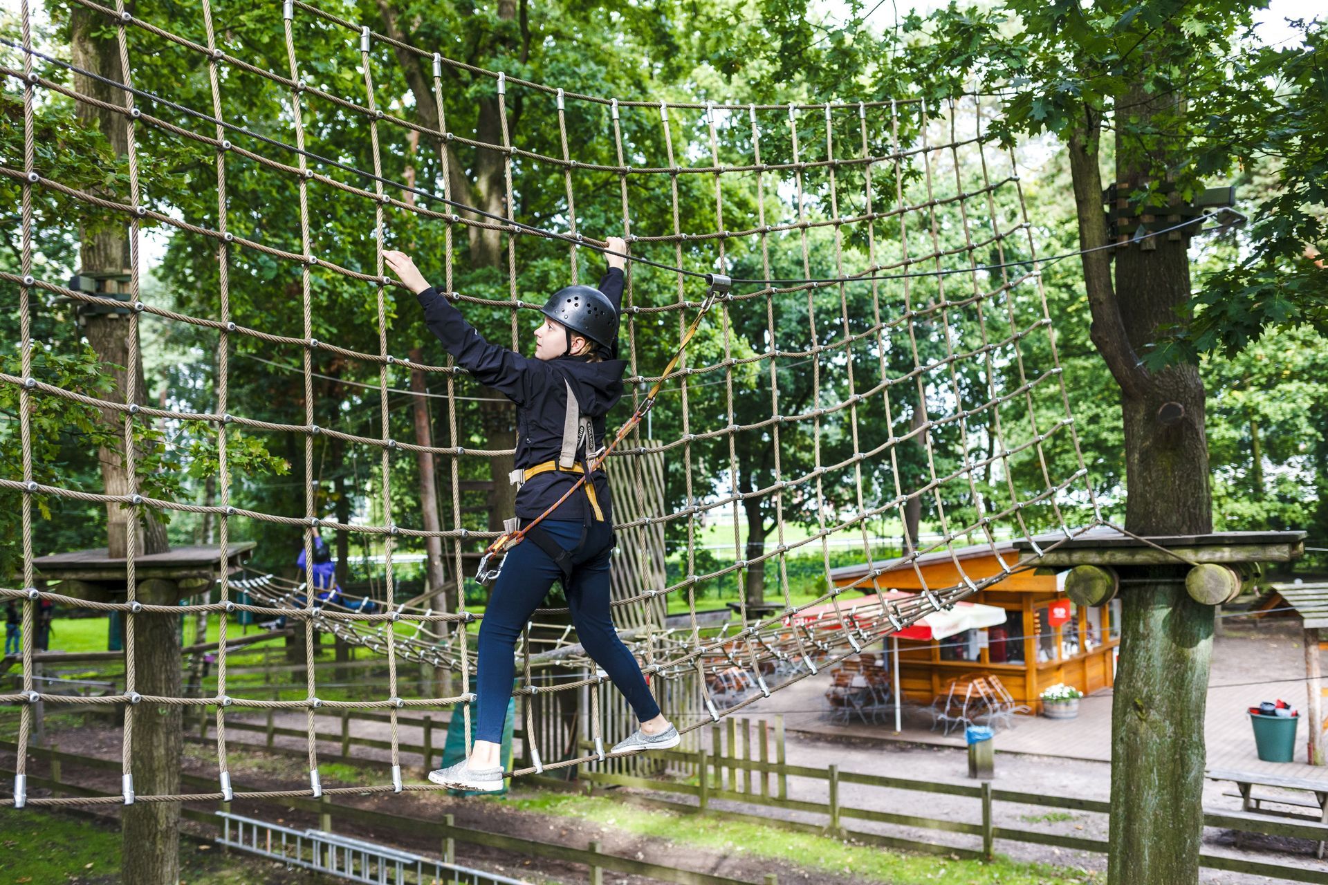 Eine Frau klettert in einem Park einen Hochseilgarten hinauf.