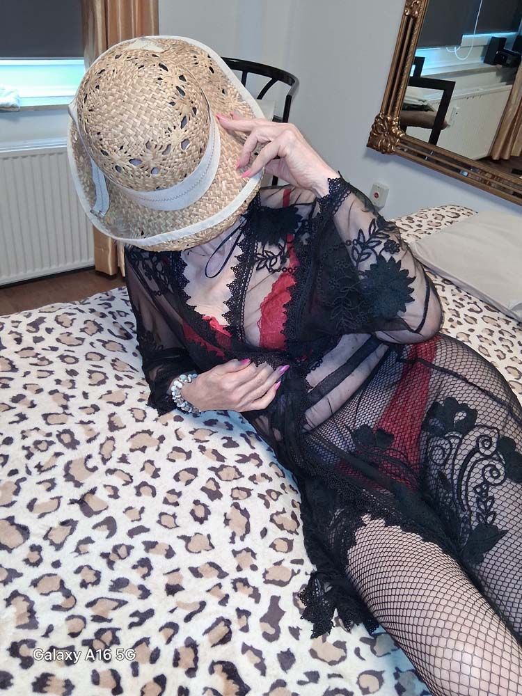 Eine Frau liegt mit Hut und Netzstrümpfen auf einem Bett.