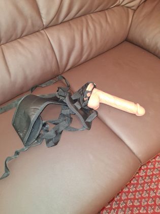 Schwarzer BH mit beigem Dildo auf einem braunen Ledersofa