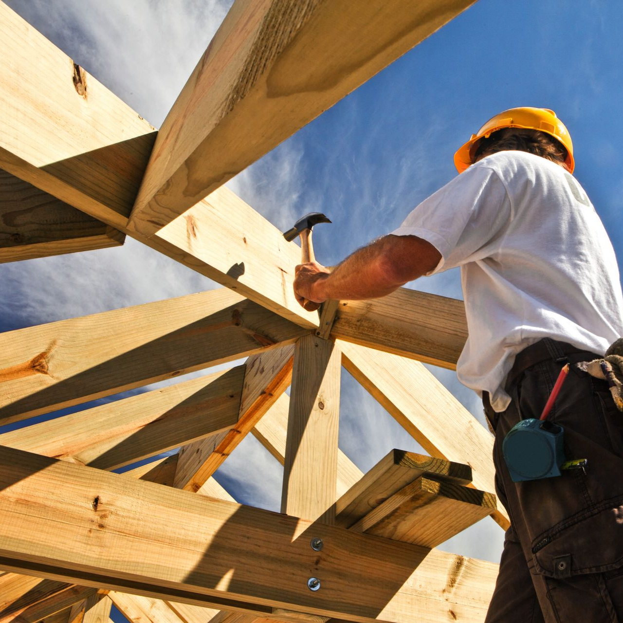 Un charpentier portant un casque de chantier martelant des poutres en bois sur un chantier de construction.