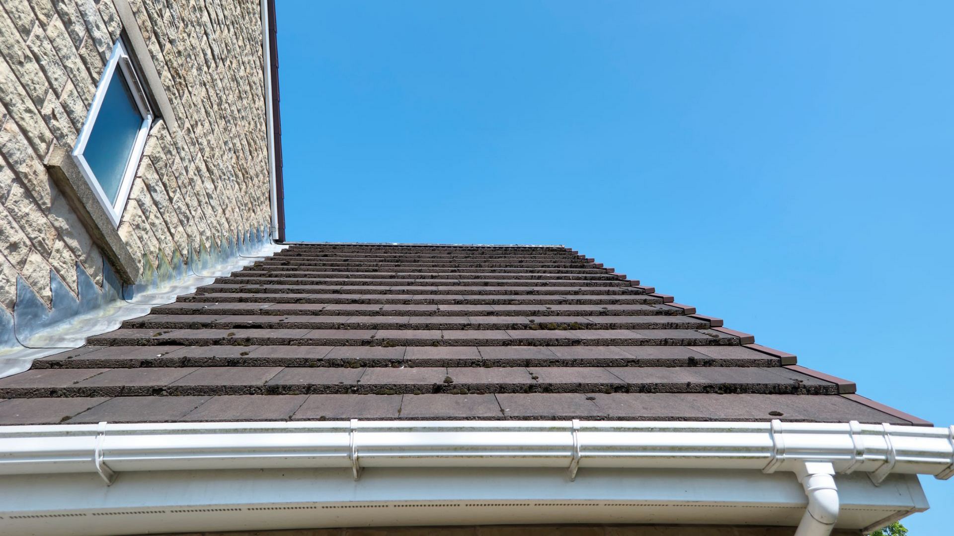 Toit de tuiles brunes avec gouttières blanches.