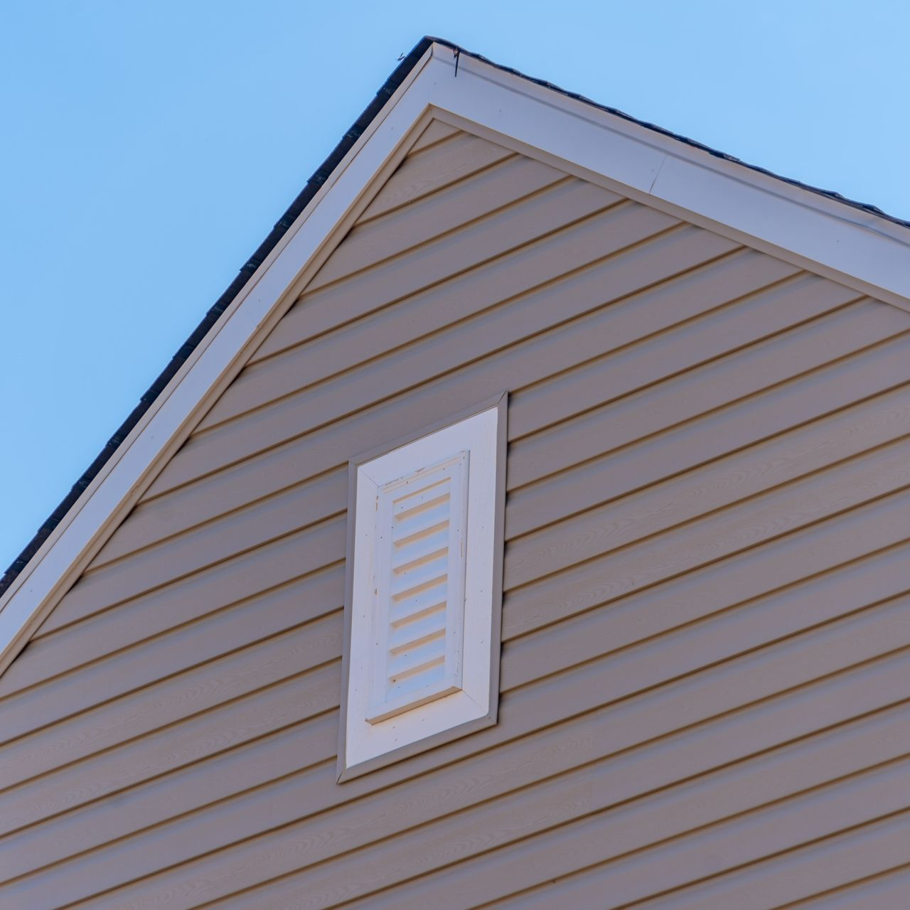 Une maison avec bardage beige, garnitures blanches et grille d'aération rectangulaire.