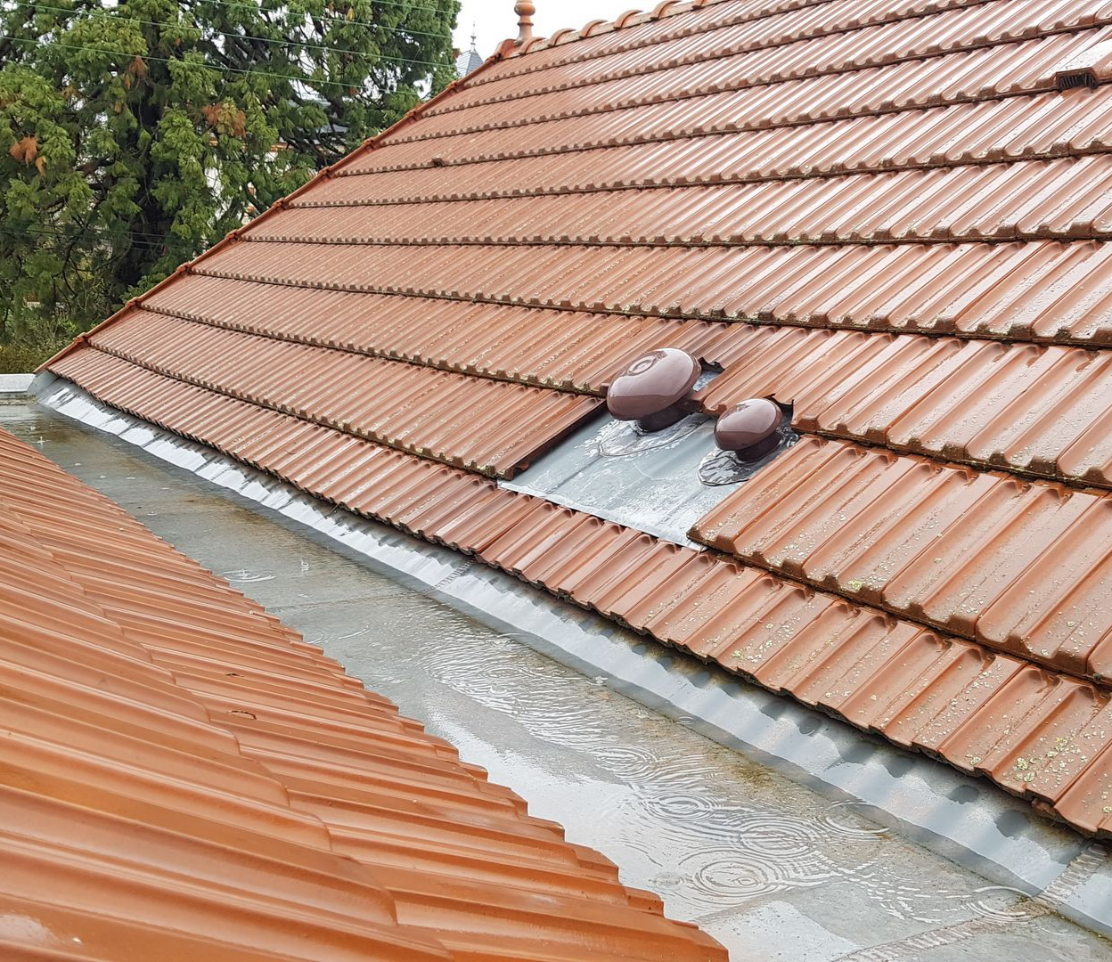 Toiture pluvieuse avec tuiles orange et gouttière remplie d'eau.