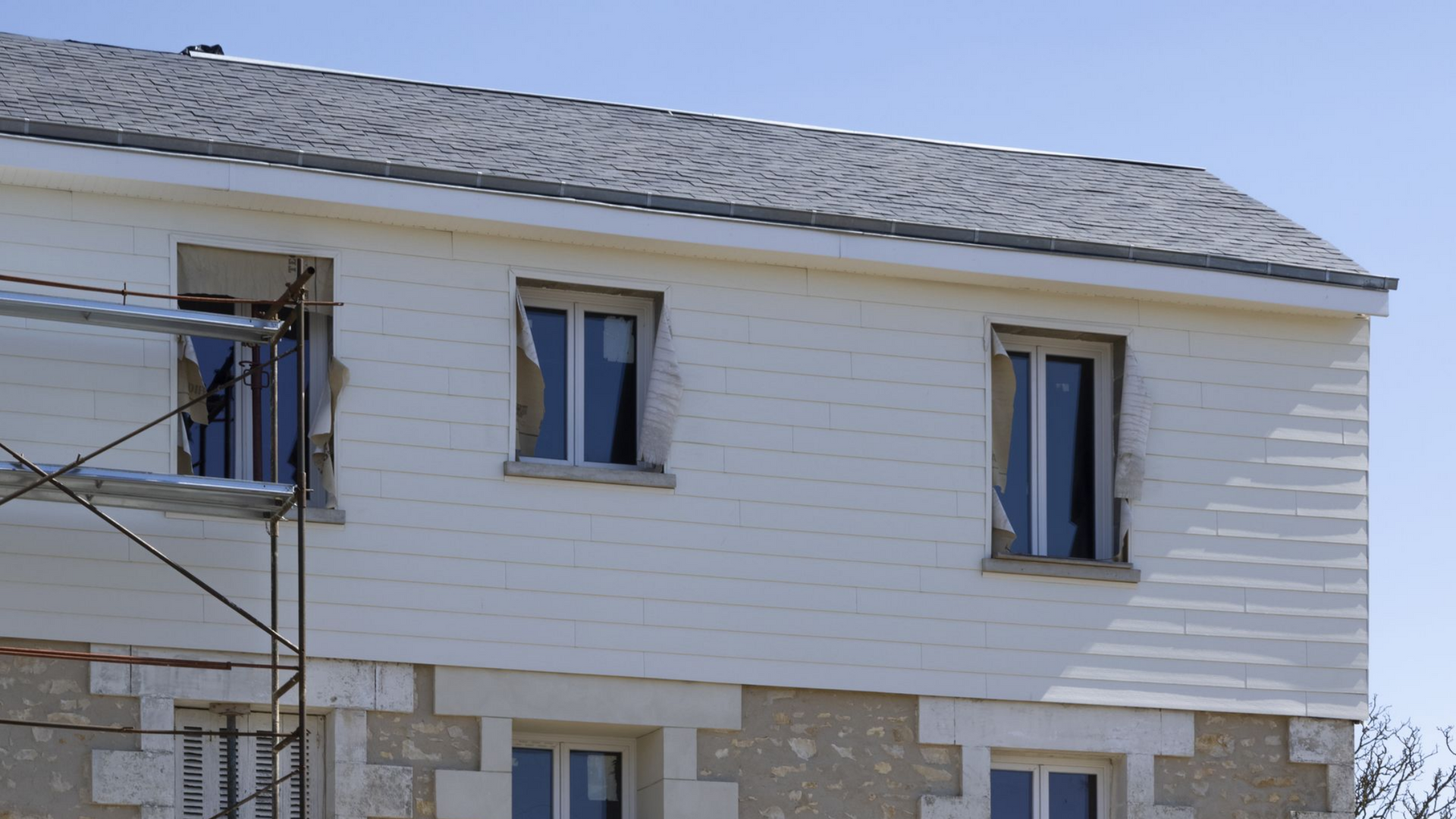 Extérieur de maison blanche avec trois fenêtres, échafaudages.