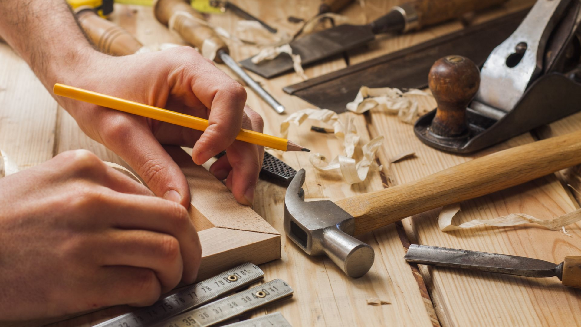 Des mains utilisant un crayon pour marquer du bois, entourées d'outils de menuiserie.