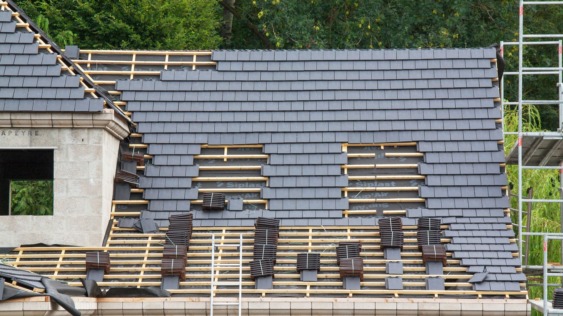 Toiture d'un bâtiment en construction, partiellement recouverte d'ardoises gris foncé.