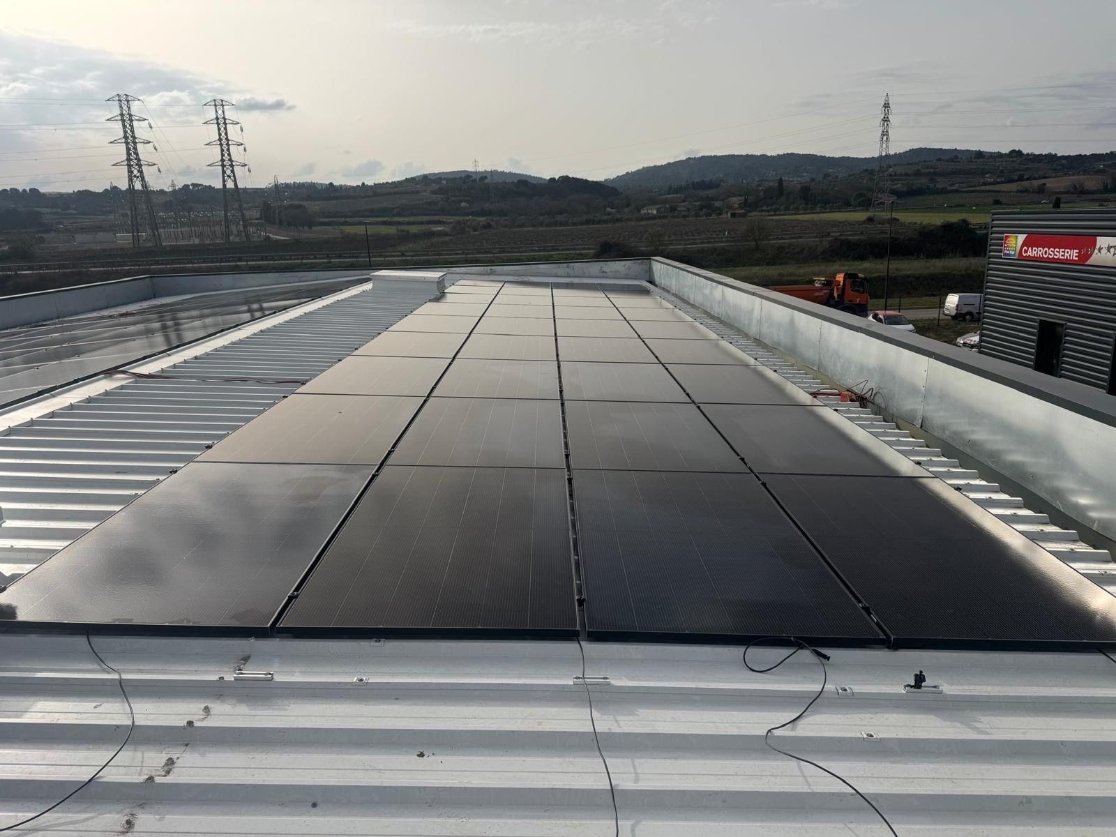 Vue d'un toit-terrasse montrant un grand nombre de panneaux photovoltaïques noirs installés sur un toit en tôle ondulée blanche