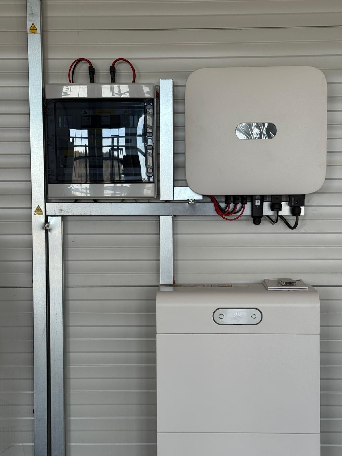 Un onduleur solaire mural, une batterie correspondante et une boîte de jonction électrique reliés par une structure métallique