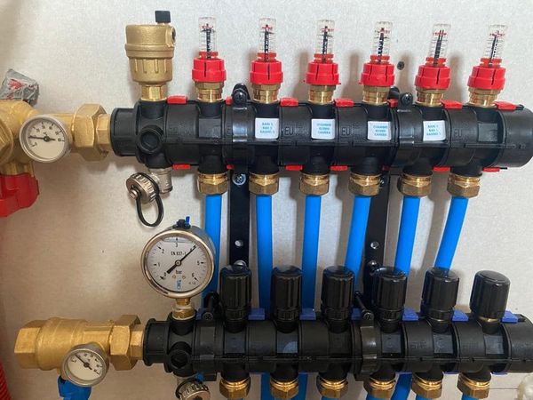 Collecteur de chauffage par le sol radiant hydronique avec collecteurs en plastique noir, tuyauterie bleue, débitmètres rouges et manomètres