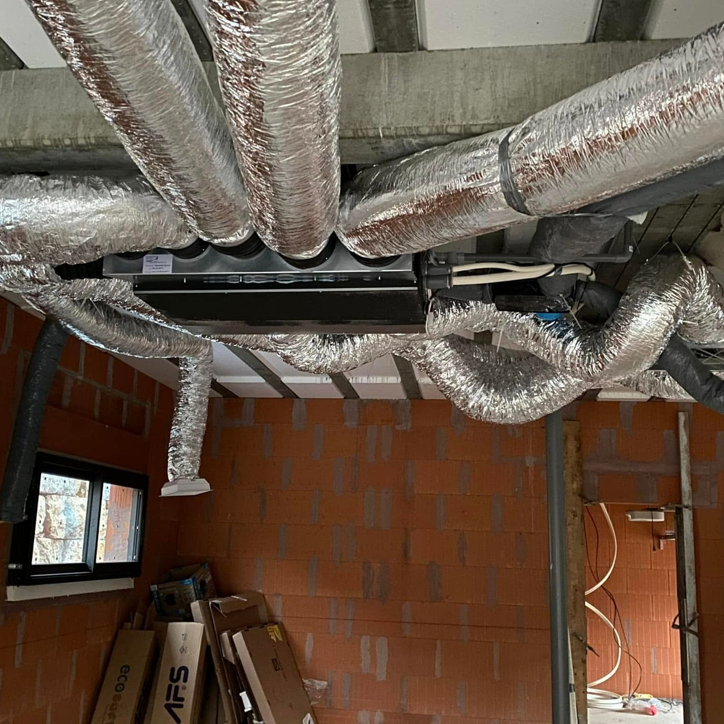 Conduits d'air de climatisation recouverts de papier aluminium, fixés à une unité montée au plafond dans une pièce aux murs de briques rouges