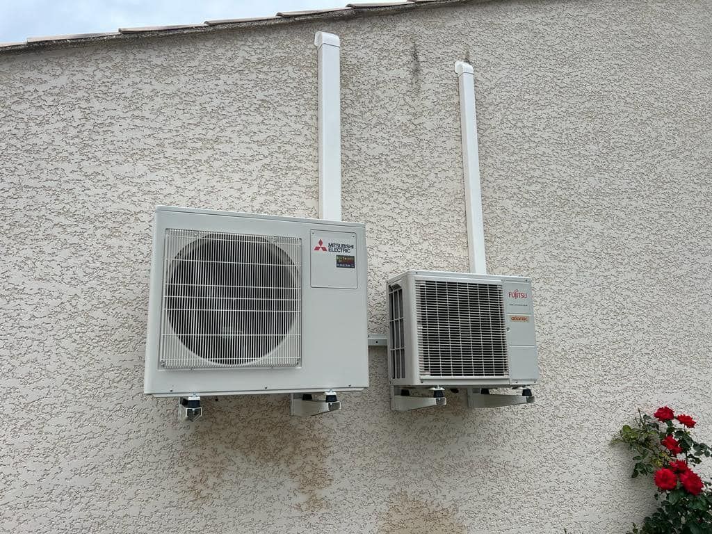 Deux unités de condensation de climatisation Mitsubishi blanches, montées sur un mur extérieur avec tuyauterie verticale