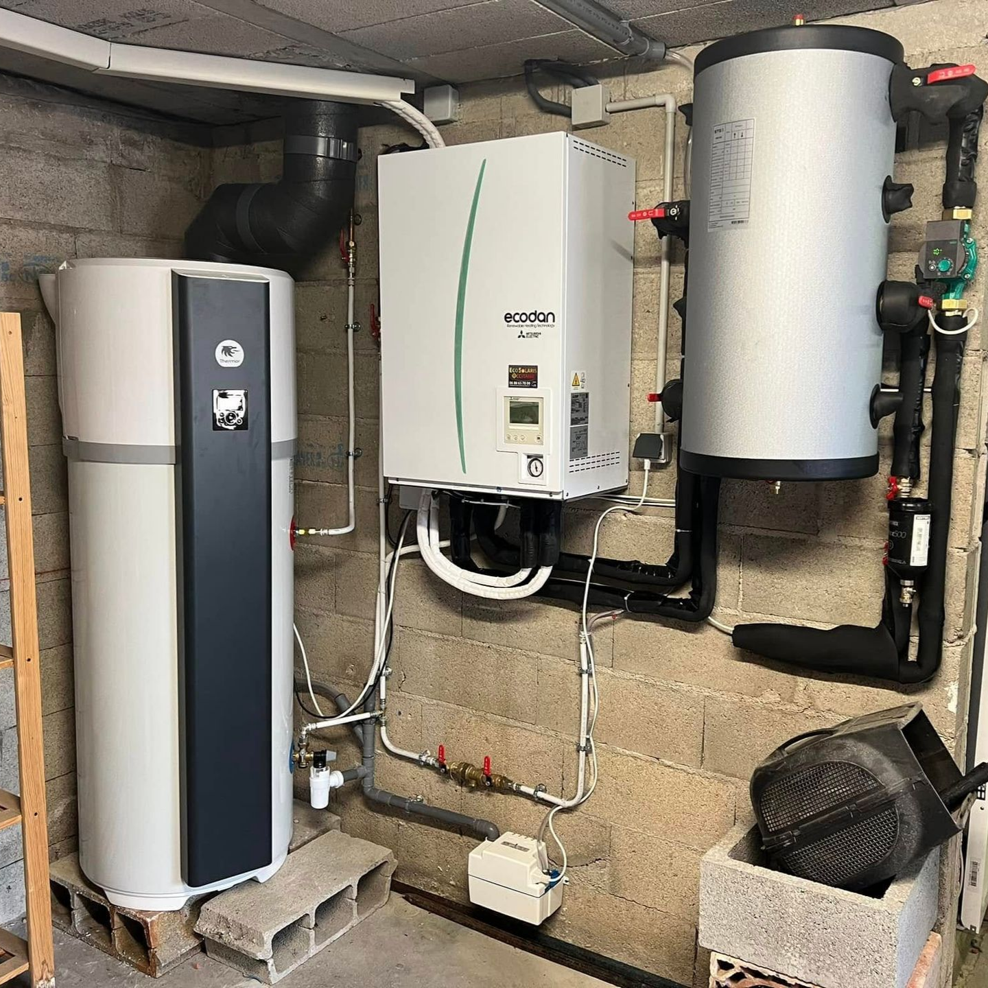 Une chaudière murale blanche et deux réservoirs d'eau cylindriques installés dans une buanderie au sous-sol