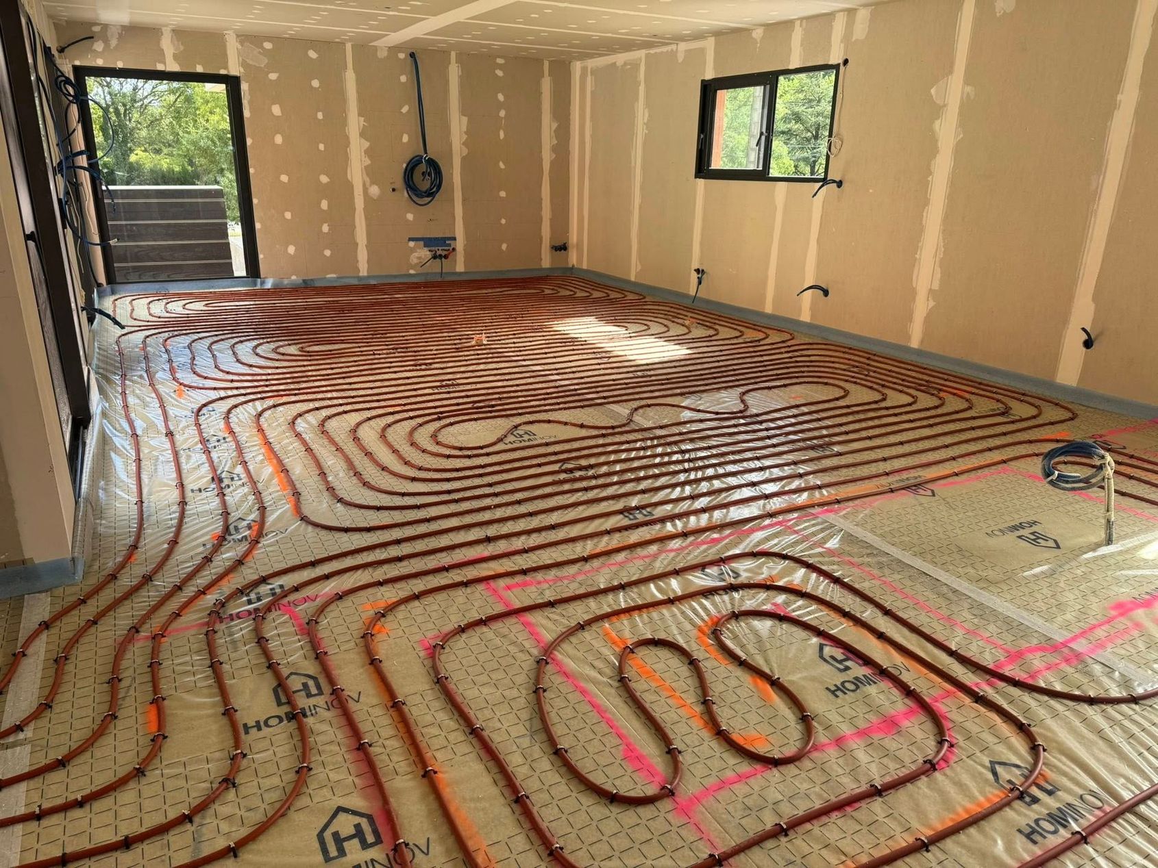 Intérieur d'une pièce en construction avec des tuyaux de chauffage au sol radiant installés sur une base en treillis et des murs non finis