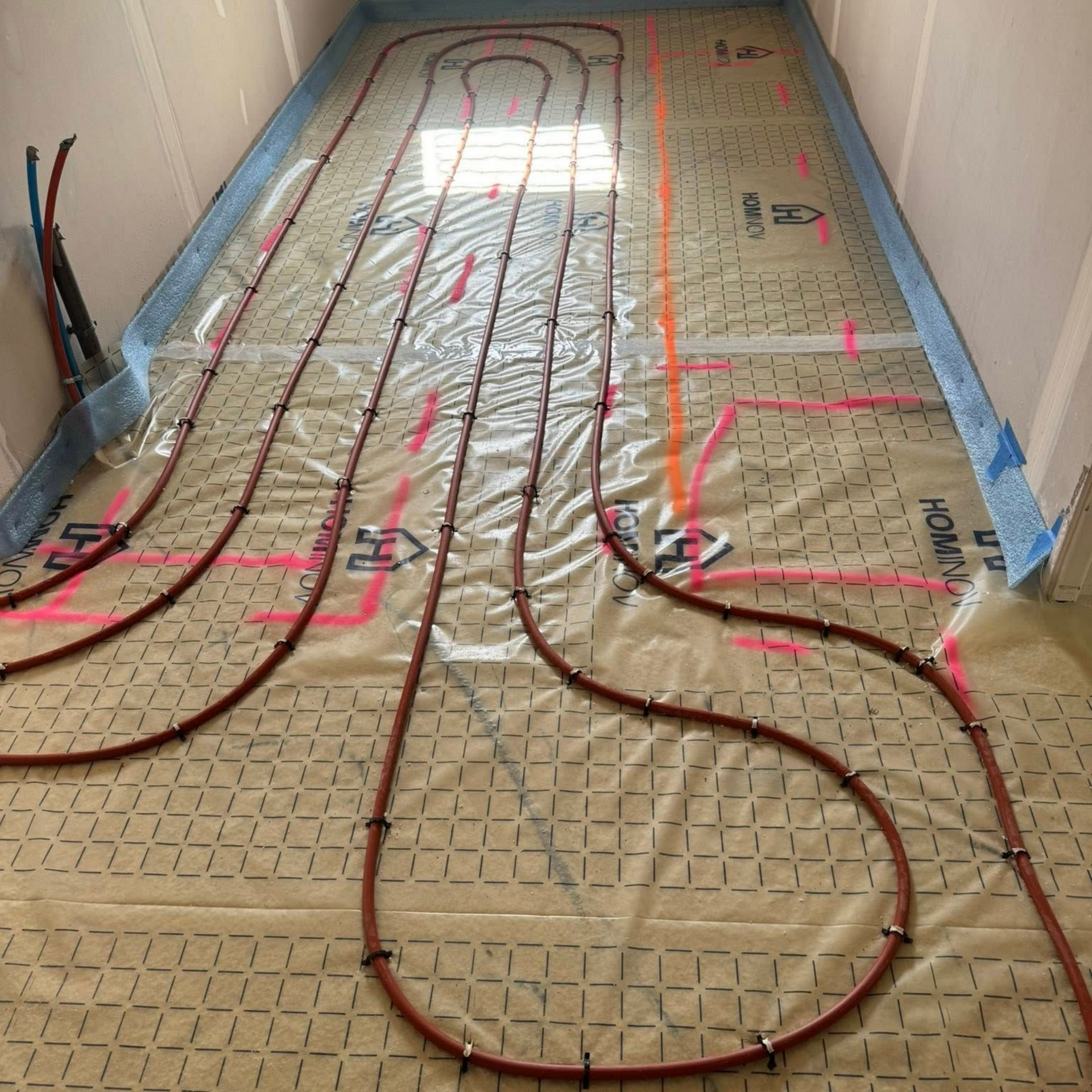 Des tuyaux de chauffage au sol sont installés selon une grille au-dessus de l'isolant dans une pièce en construction