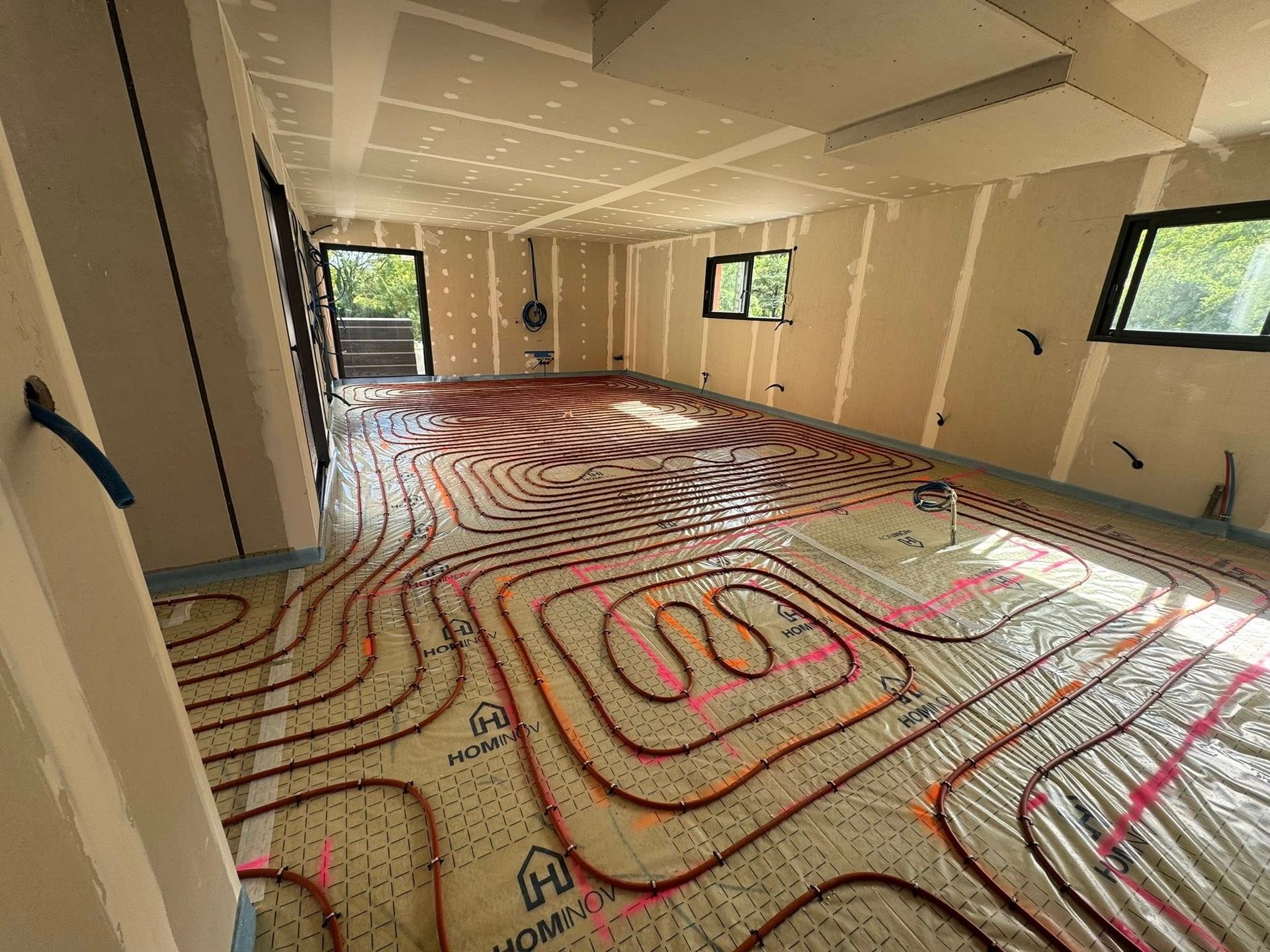 Des tuyaux de chauffage au sol radiant rouges sont installés en spirale dans une pièce en construction aux murs nus