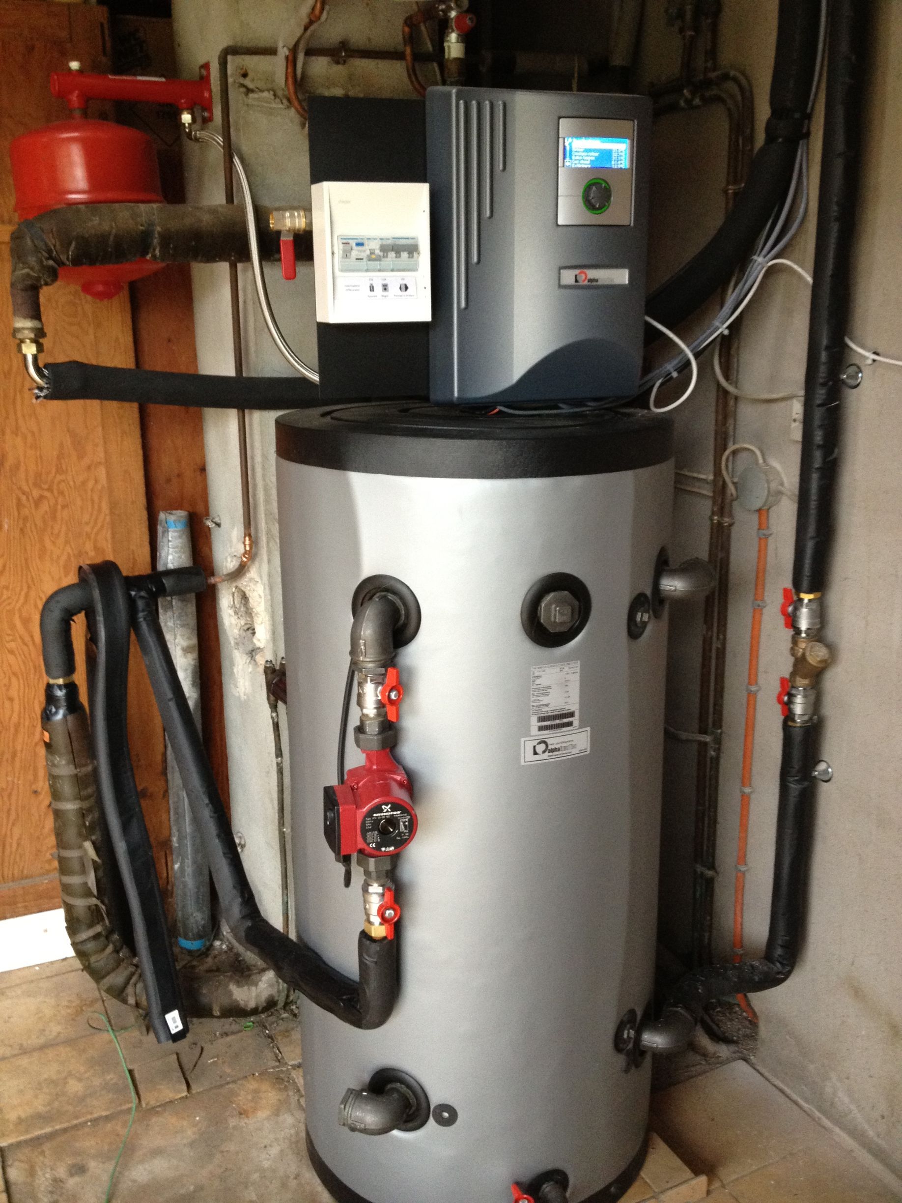 Un ballon d'eau chaude argenté avec une unité de commande numérique montée sur le dessus et des tuyaux isolés