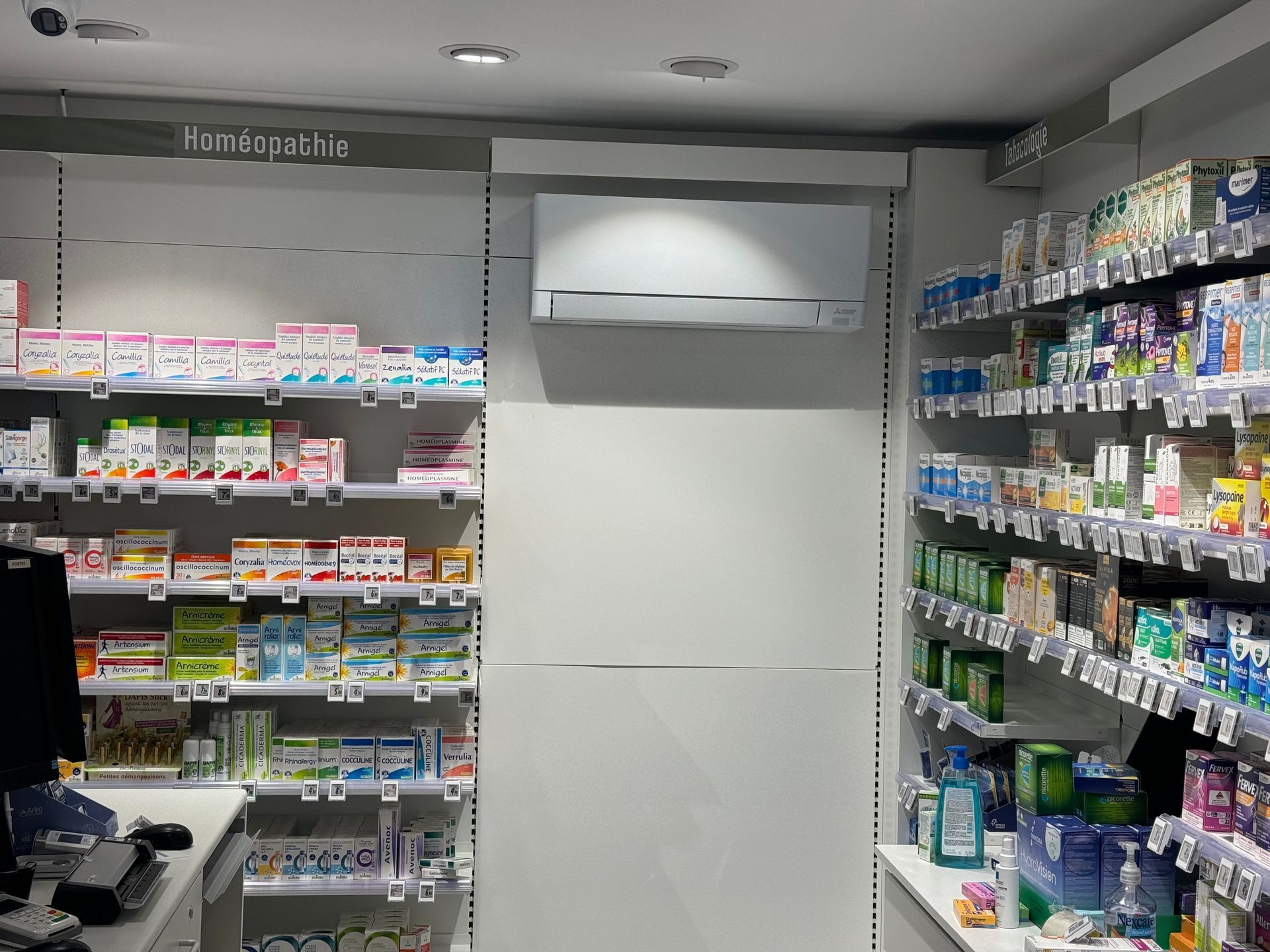 Climatiseur mural installé dans les rayons d'une pharmacie, juste en-dessous du plafond