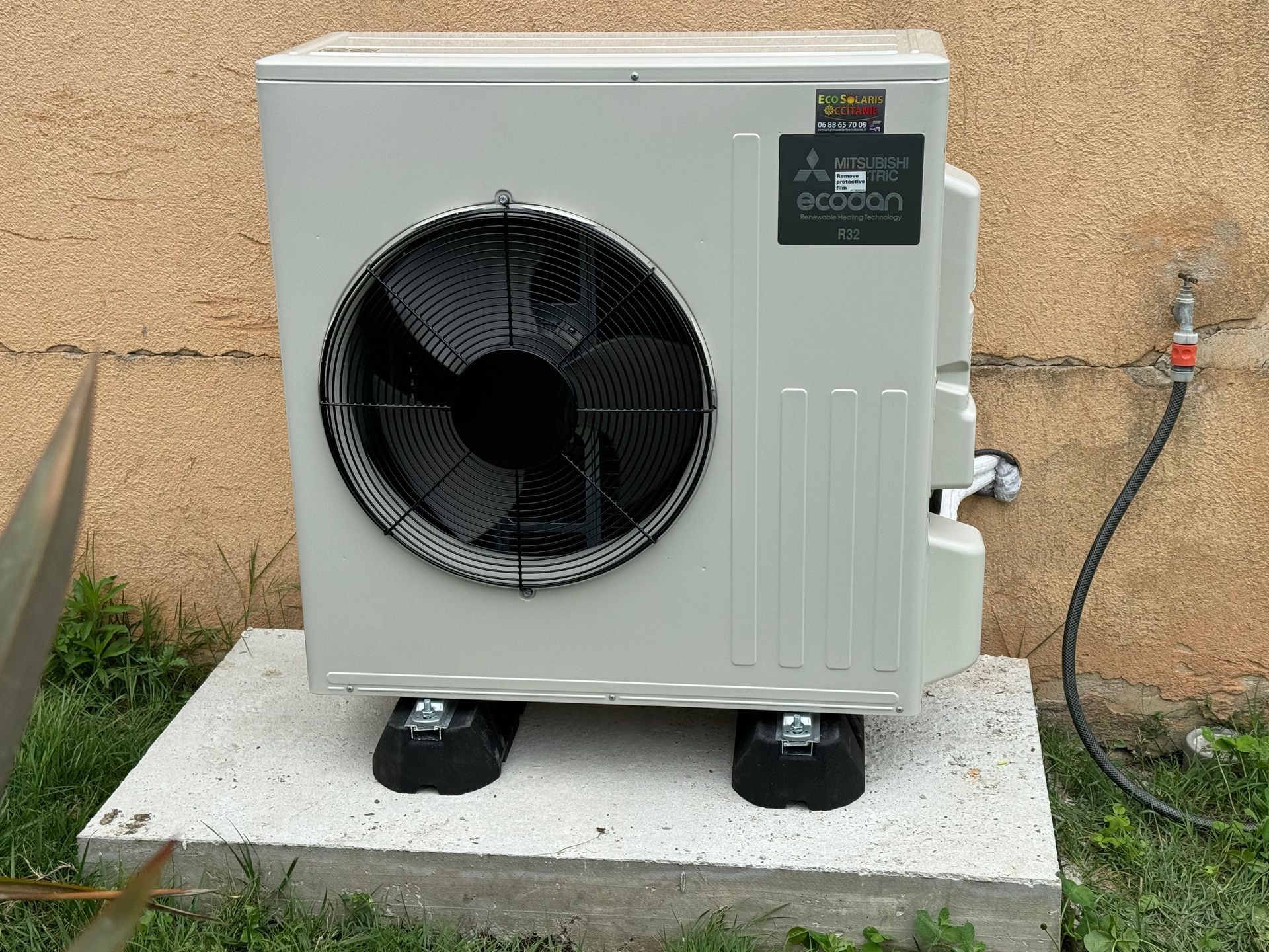 Unité de pompe à chaleur extérieure gris clair, montée sur une dalle de béton contre un mur extérieur texturé