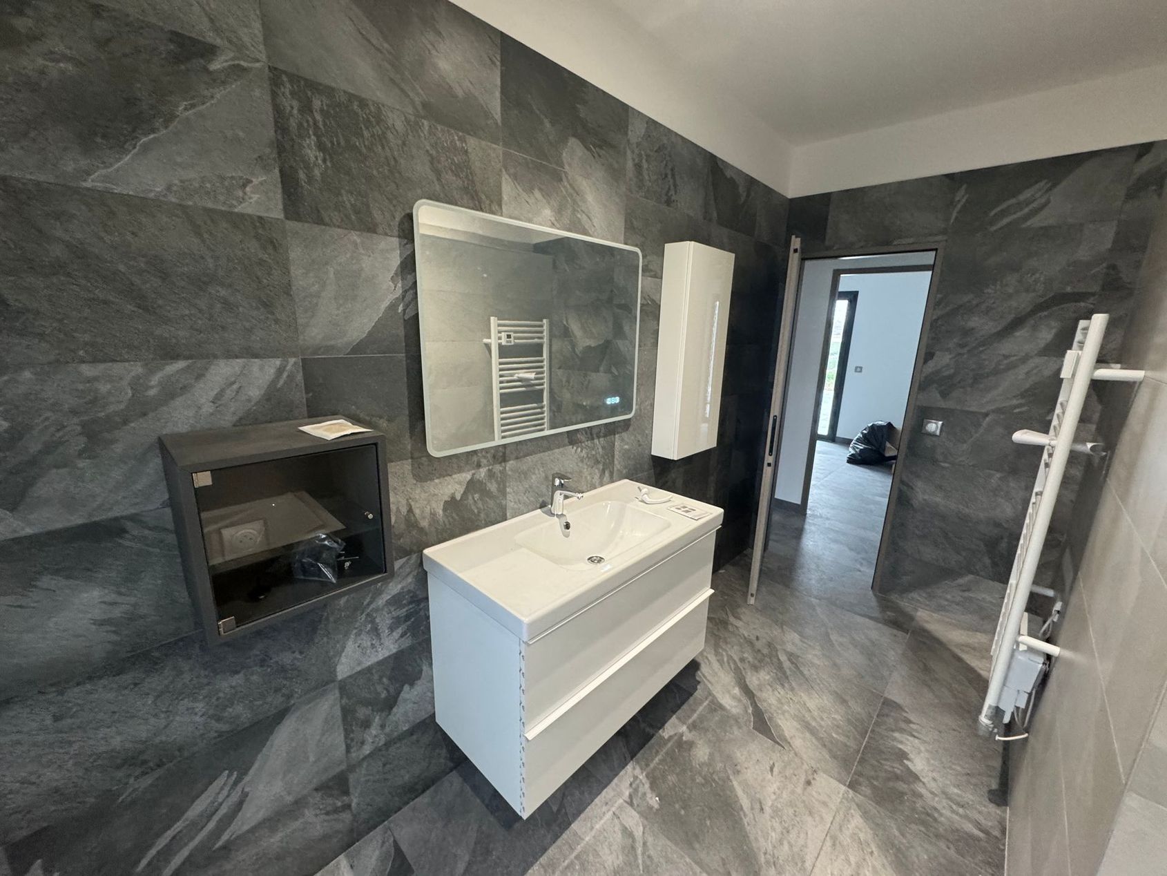 Salle de bains avec murs et sol en marbre, meuble vasque blanc, miroir et sèche-serviettes