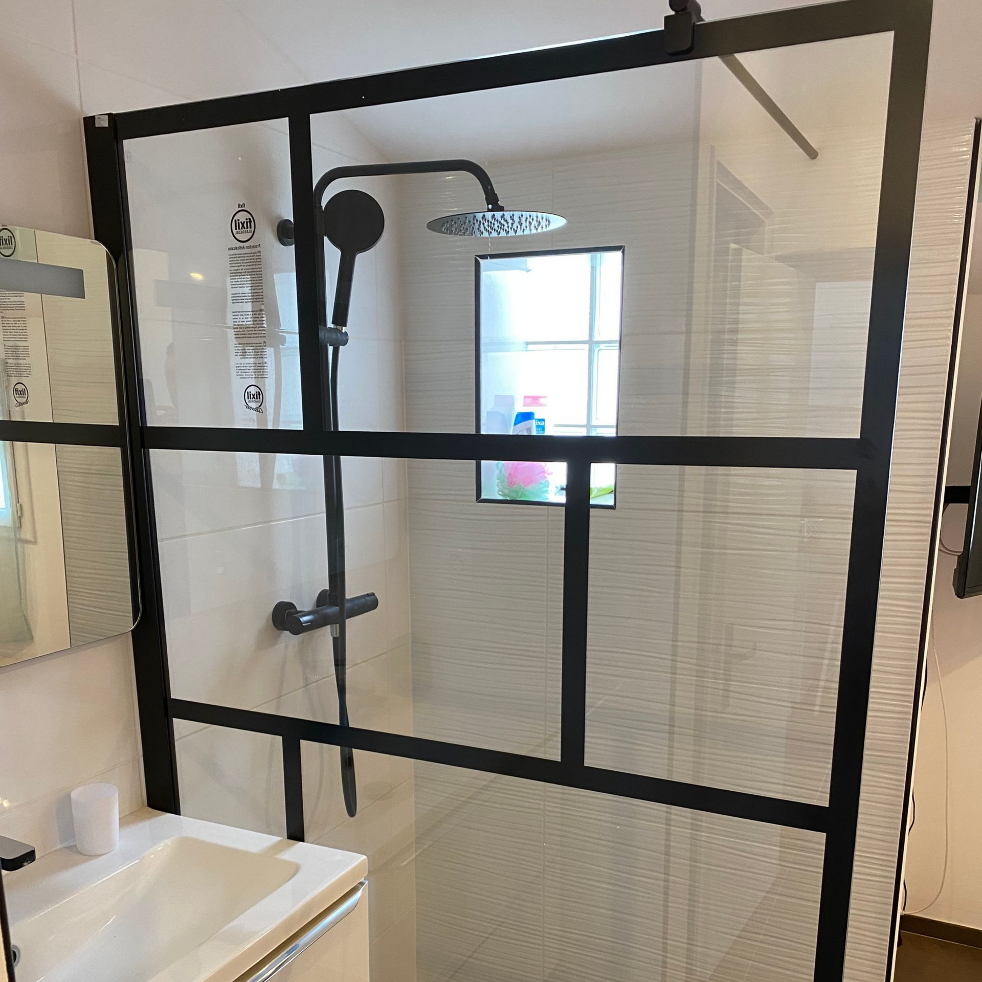 Une douche à l'italienne avec un cadre noir et des parois en verre transparent