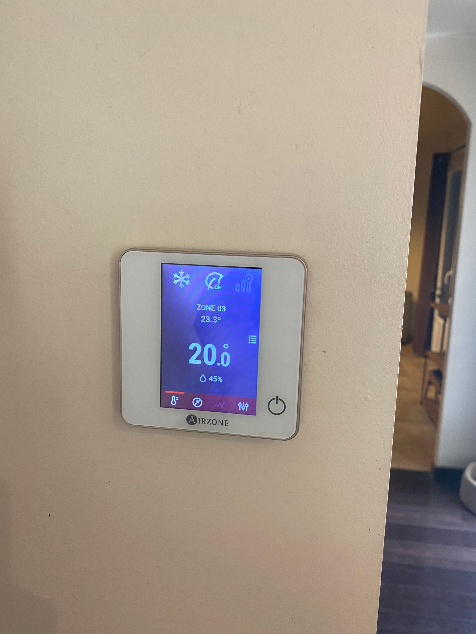 Un thermostat numérique blanc, fixé sur un mur beige, affiche une température de 20 degrés Celsius