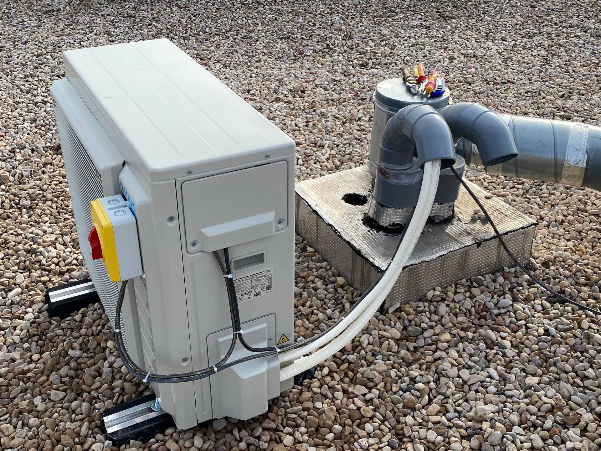 Un climatiseur sur un toit en gravier, relié à des tuyaux de raccordement