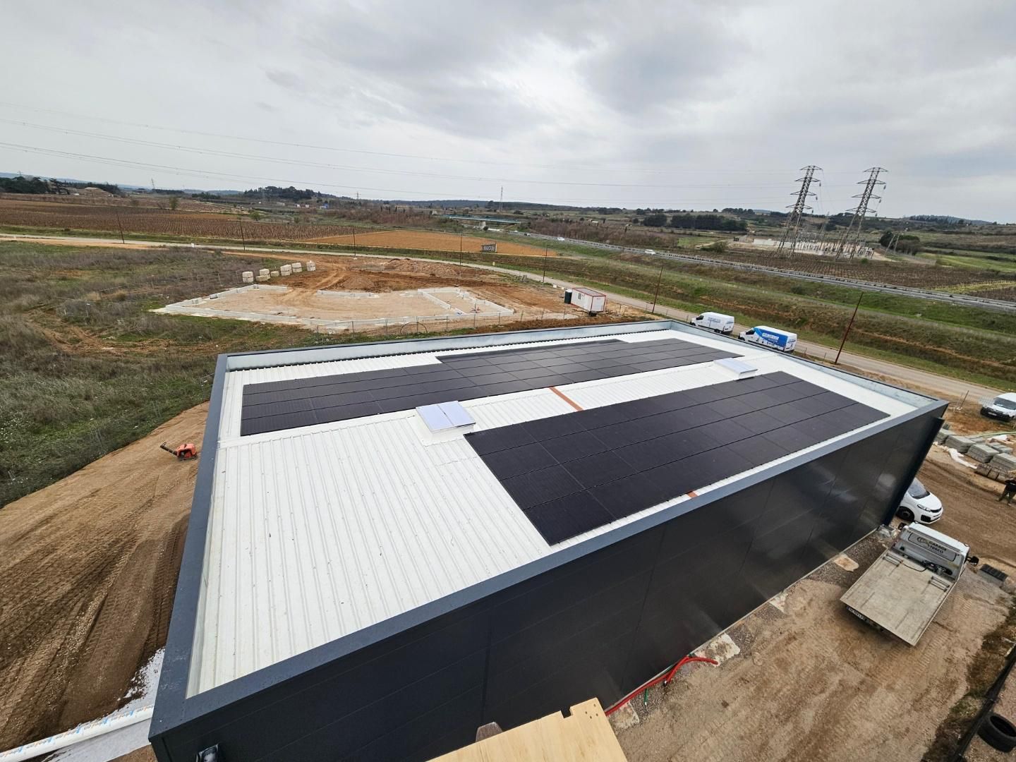 Vue aérienne du toit rectangulaire d'un entrepôt, sur lequel on distingue deux grands panneaux photovoltaïques sombres