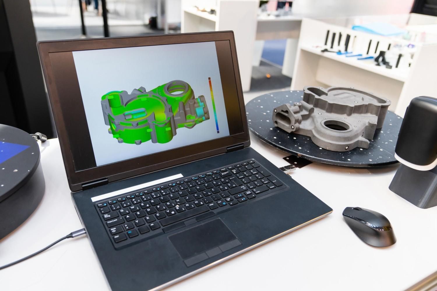 La computadora portátil muestra un modelo 3D con un escáner y un objeto. El objeto está sobre una plataforma giratoria.