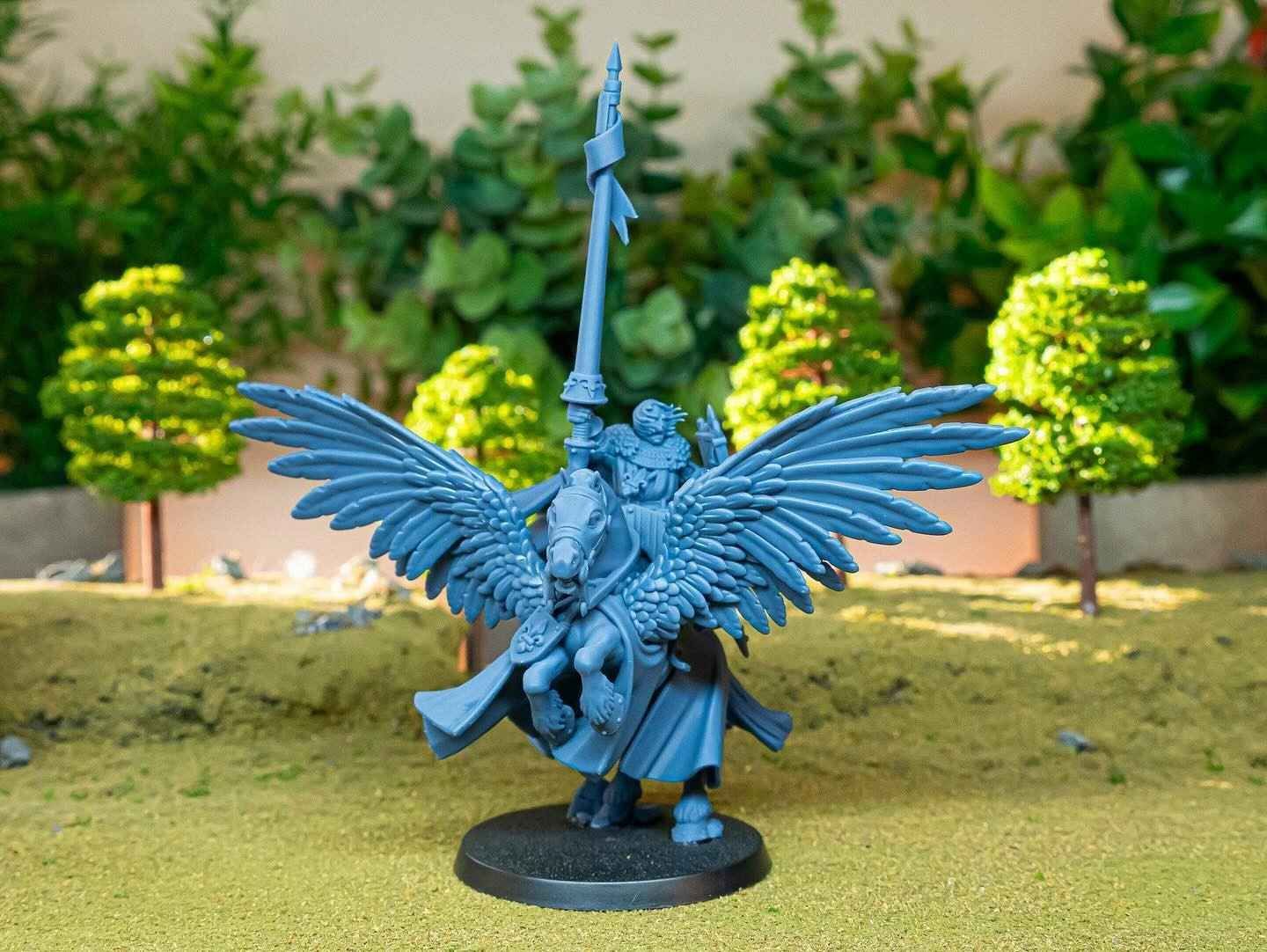 Figura en miniatura de caballo alado con caballero sobre peana, delante de arboles en miniatura.