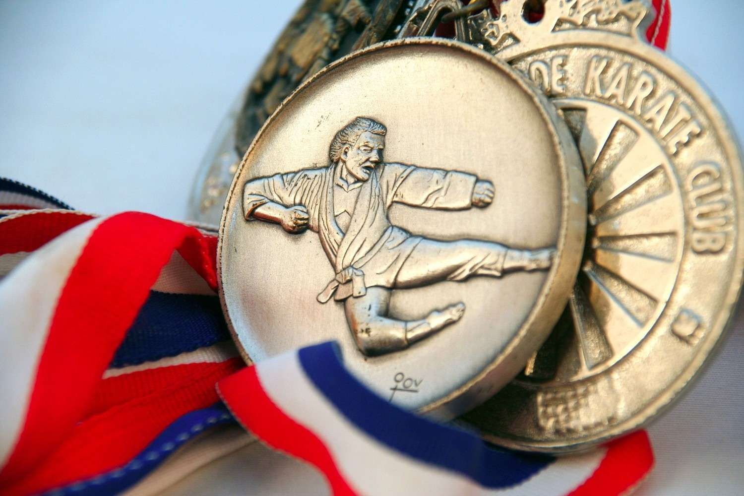 Medallas de karate con cintas rojas, blancas y azules; una de las medallas representa a un practicante de karate.