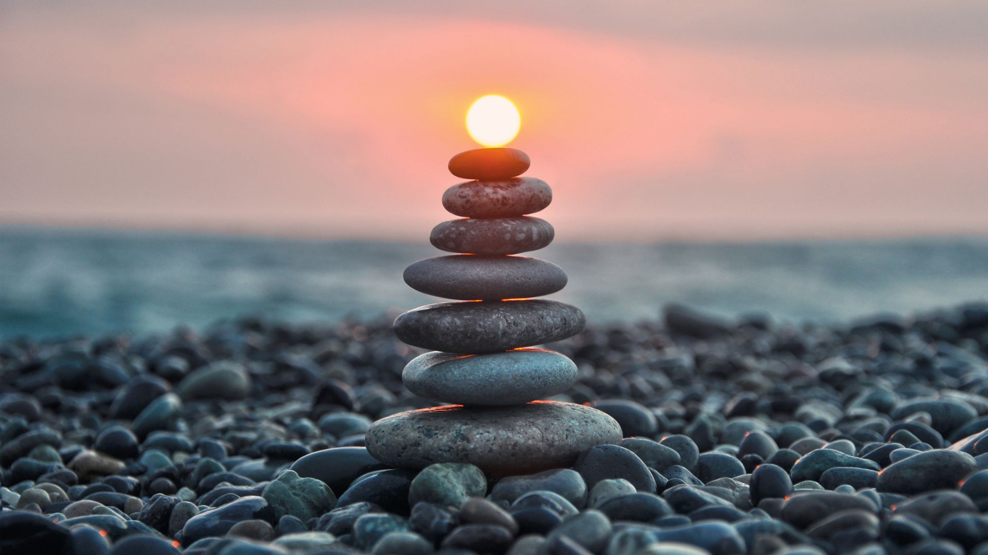 Des pierres empilées sur une plage de galets au coucher du soleil, le soleil aligné au-dessus de la pierre supérieure.