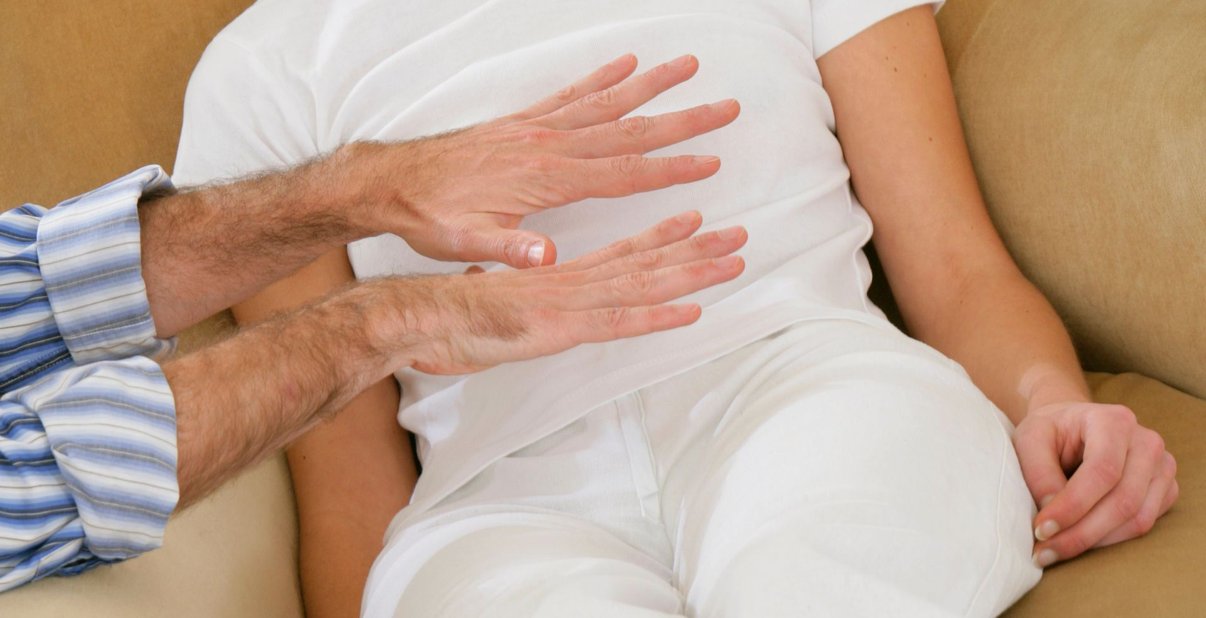 Deux mains font des gestes tandis qu'une personne est assise sur un canapé en tenue blanche