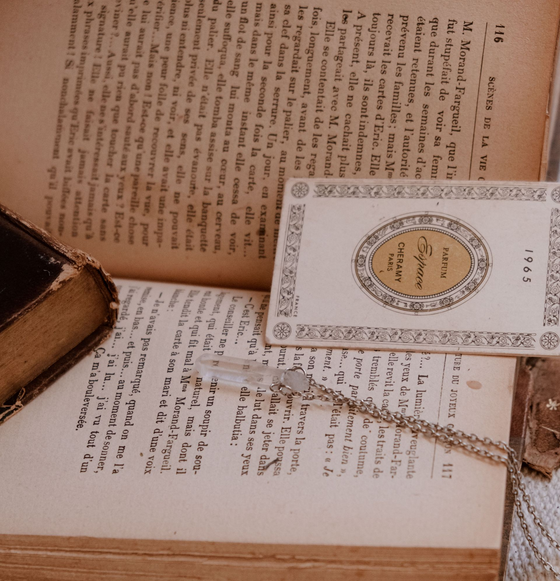 Livre ouvert avec une petite carte décorative et un stylo-plume en laiton posés dessus, vu en diagonale.